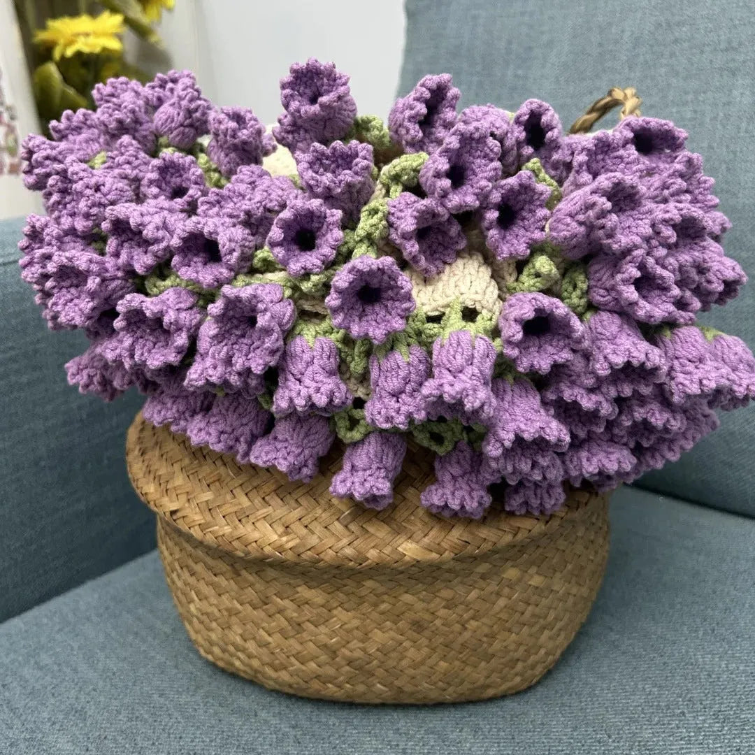 A bouquet of handmade crochet lavender flowers arranged in a woven basket, displayed on a blue sofa as a charming decorative gift.