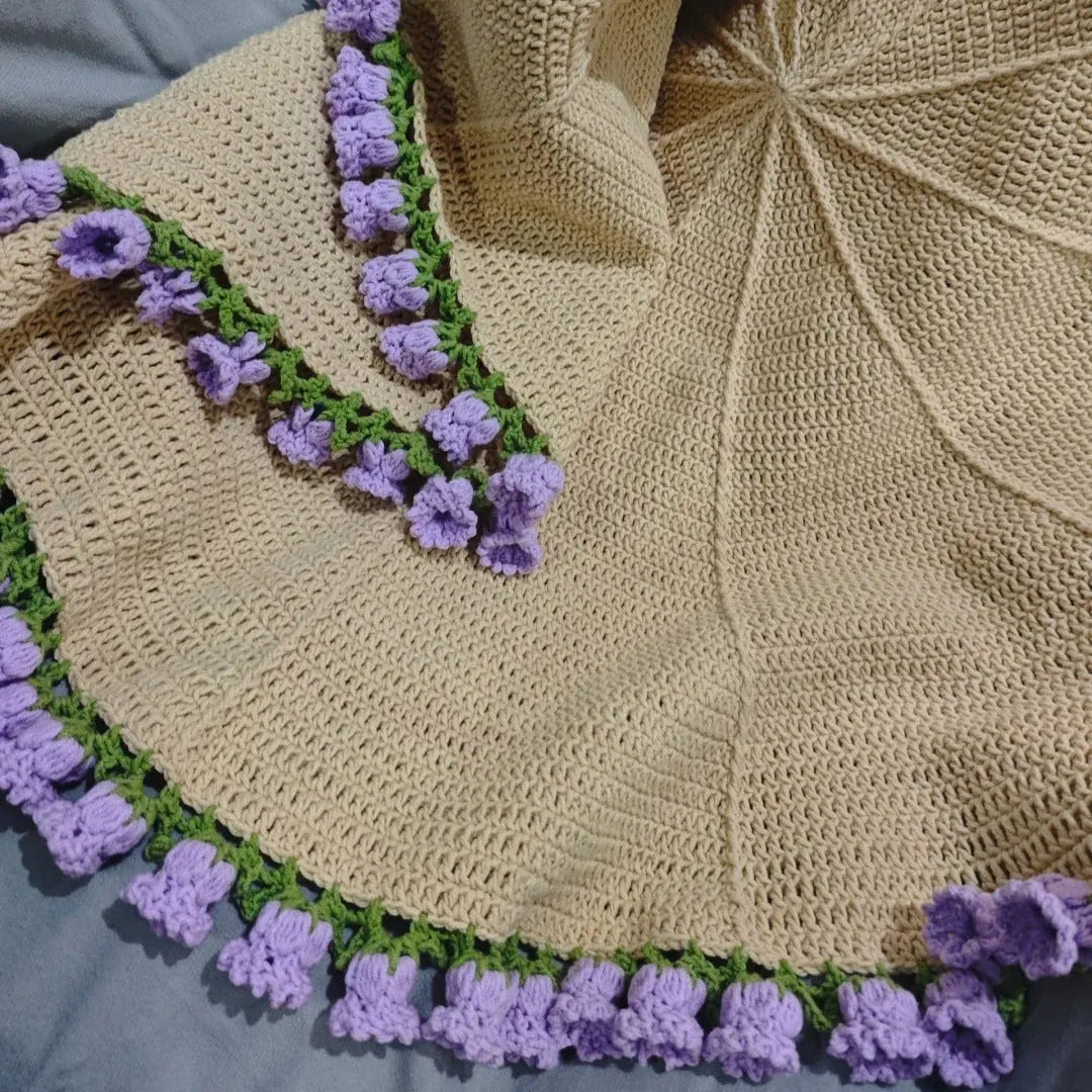 Hand-crocheted beige round blanket with purple bellflower edging, ideal for home decor and cozy gifting