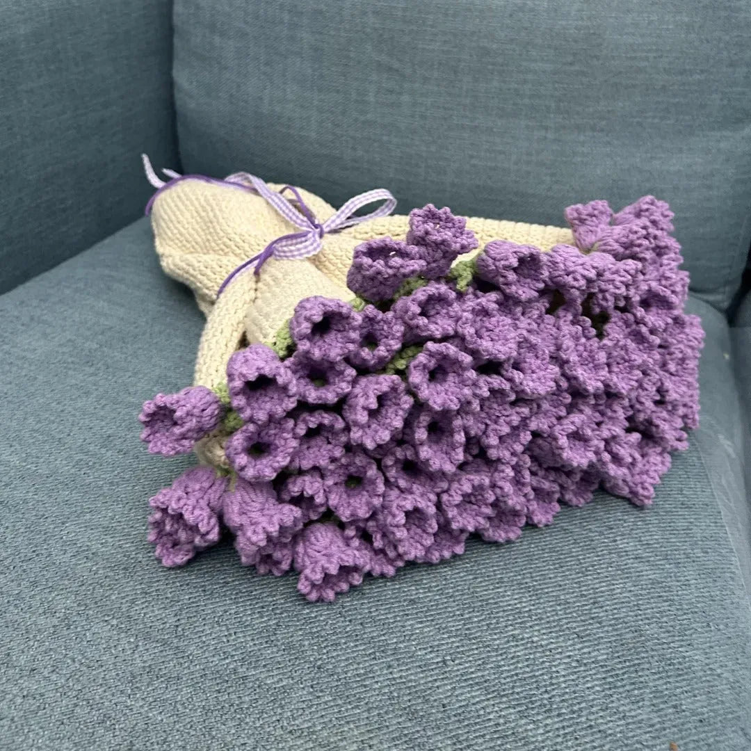 A handmade crochet blanket designed like a bouquet of blooming lavender flowers, neatly tied with a gingham ribbon, placed on a soft blue couch.