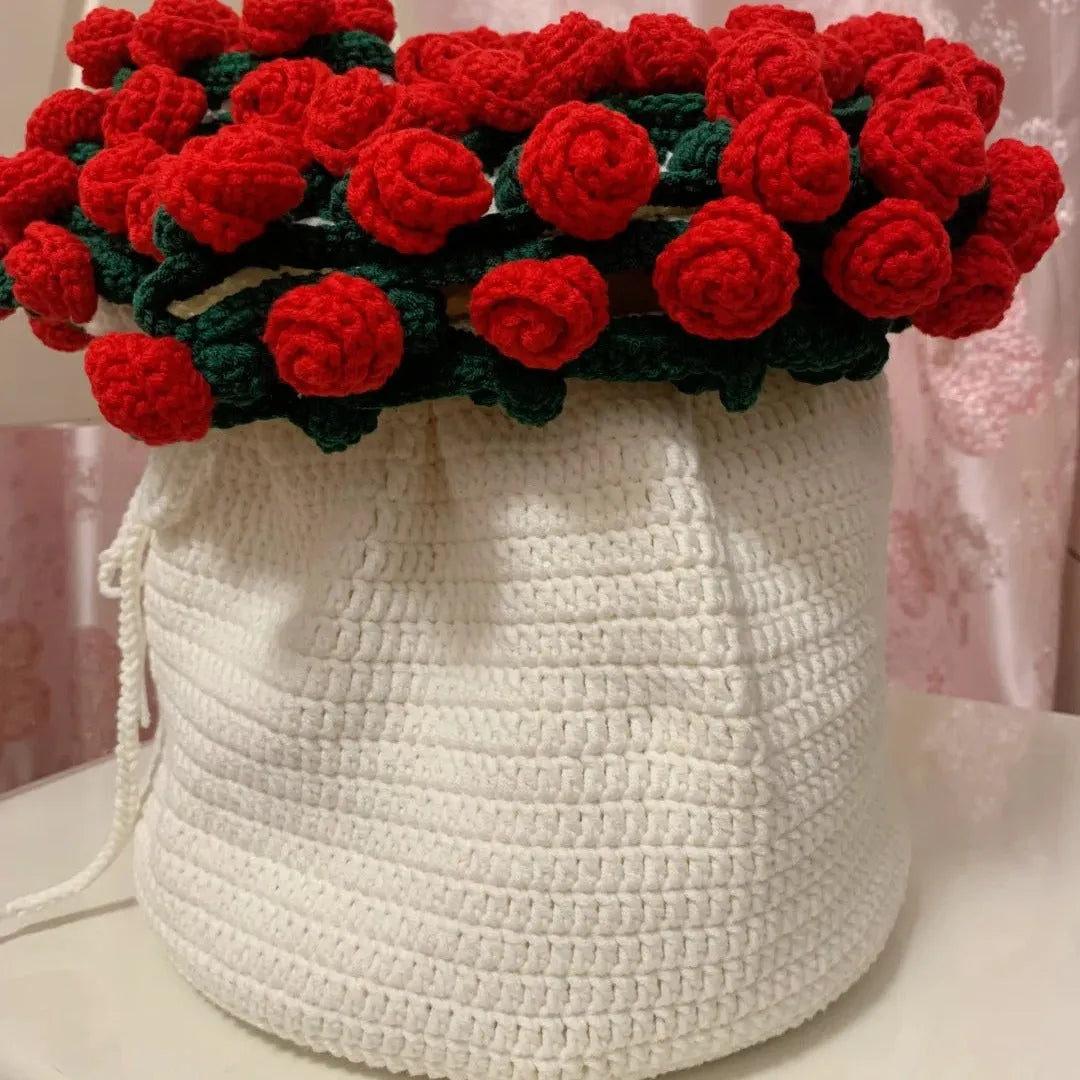 Handmade crochet blanket arranged in a drawstring pouch shape with vivid red roses and green leaves on top, showcasing a gift-like bouquet presentation