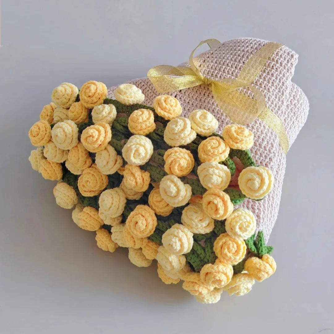 A beautifully wrapped handmade crochet blanket featuring a bouquet-style arrangement of yellow and cream 3D crochet roses with green leaves and a golden ribbon, styled as a gift on a clean gray background